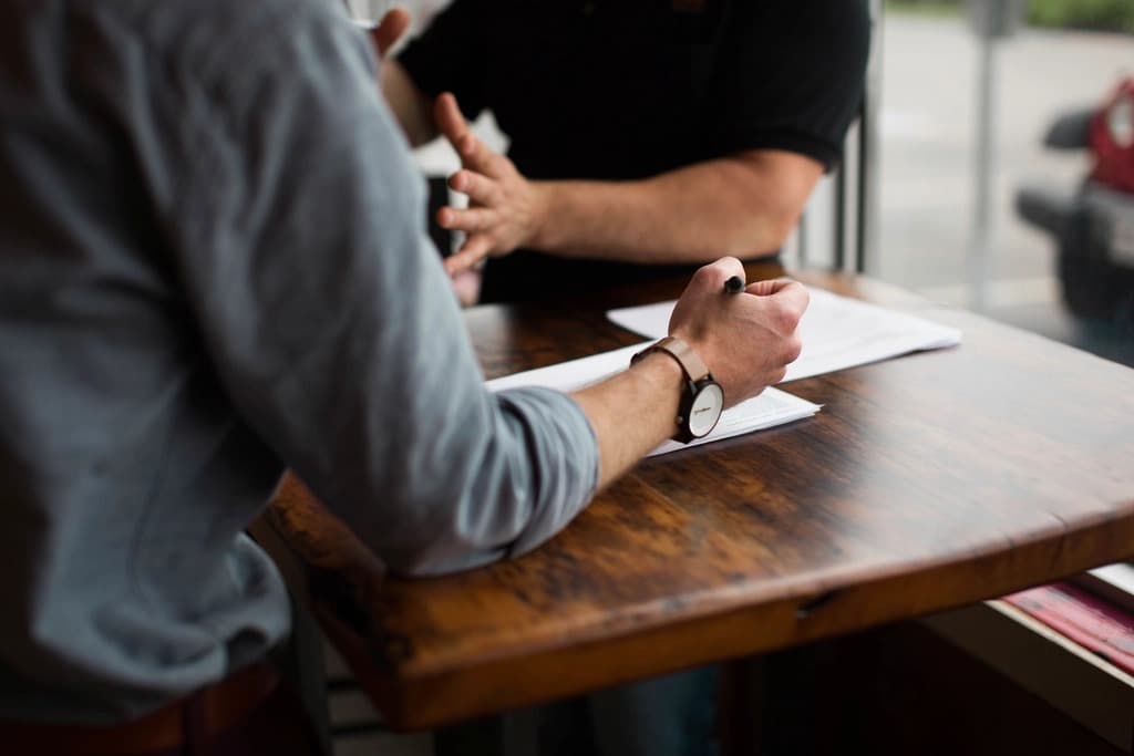 Deux professionnels examinant un document contractuel de part et d’autre d’une table